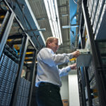 IT administrator installing a new rack mount server. Large scale storage server is also seen.