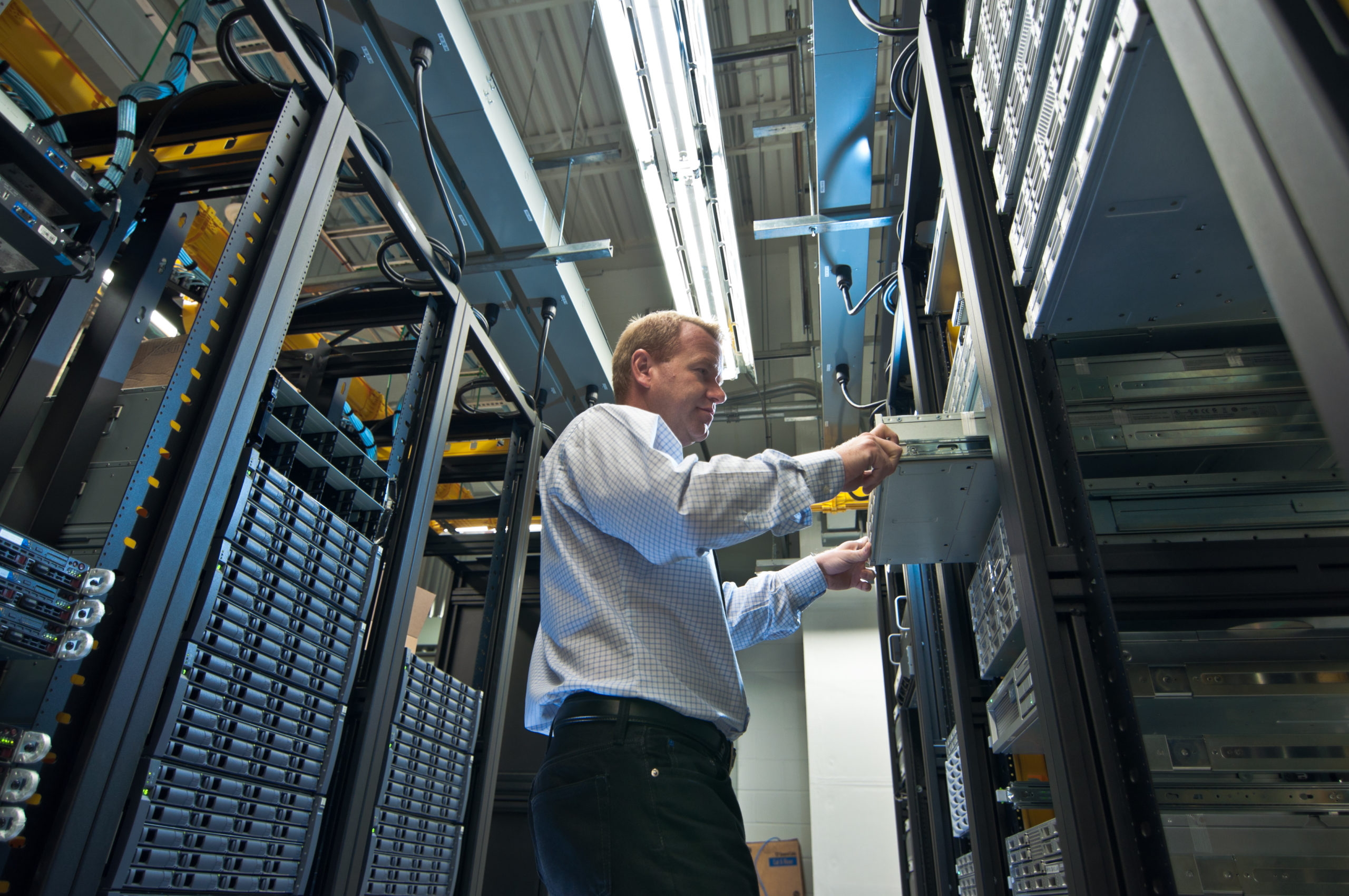 IT administrator installing a new rack mount server. Large scale storage server is also seen.