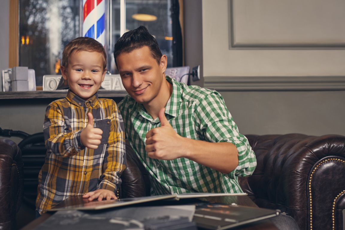 A young father and his stylish little son in a barbershop waiting room.